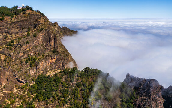 Aerial view of Cova Crater Panoramic Viewpoint featuring rugged volcanic cliffs, lush green vegetation, and a sea of clouds filling the crater in Faja de Cima, Porto Novo, Cabo Verde.