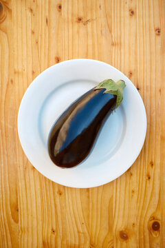 Fresh eggplant on white plate over rustic wooden table