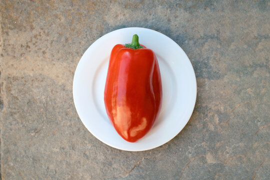 Red bell pepper on white plate against rustic background