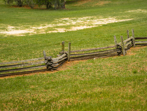 Rustic weathered wooden split rail fence made of rough logs standing on the green grass lawn inside the outdoor public park recreation area.