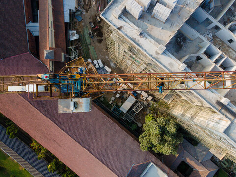 Aerial view of a construction site featuring a large crane, scaffolding, and building structures surrounded by lush trees in Banyumas Regency, Central Java, Indonesia.