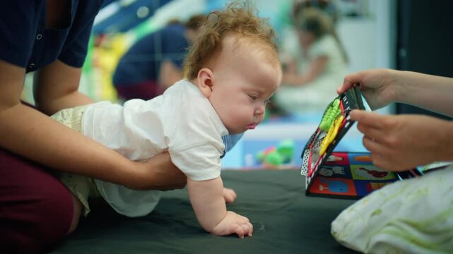 Baby practicing tummy time with adult supervision, engaging with a colorful soft book for early childhood motor skill development