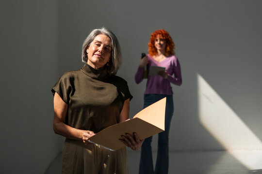 Confident mature businesswoman holding folder with colleague