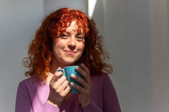 Smiling redhead woman holding blue coffee mug indoors