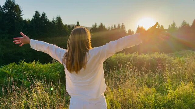 Woman with arms outstretched toward sunset in mountain forest meadow