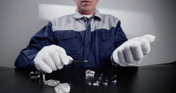 Slow motion jeweler inspecting and sorting loose diamonds on black tabletop in studio.