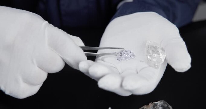 Slow motion hands placing artificial laboratory diamonds and rough crystals into gloved palm on black table.