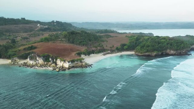 Aerial view of Pantai Watu Bella with turquoise waters, rocky cliffs, and lush green vegetation in Lamboya, East Nusa Tenggara, Indonesia.