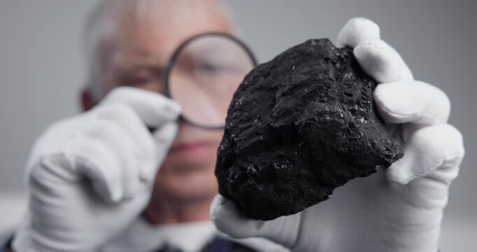 Worker miner man inspecting coal piece with magnifying glass at table.