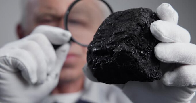 Close up of geologist inspecting black rock sample with magnifying glass in laboratory. rack focus tracking shot.