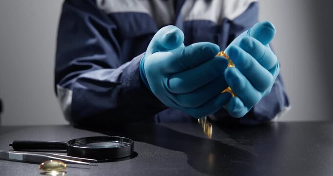 Slow motion technician hands wearing blue gloves pouring golden capsules onto black table during laboratory inspection at bench.