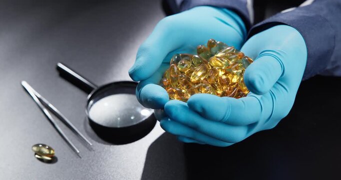 Slow motion hands holding gel capsules on lab table with magnifying glass and tweezers in clinical workspace.