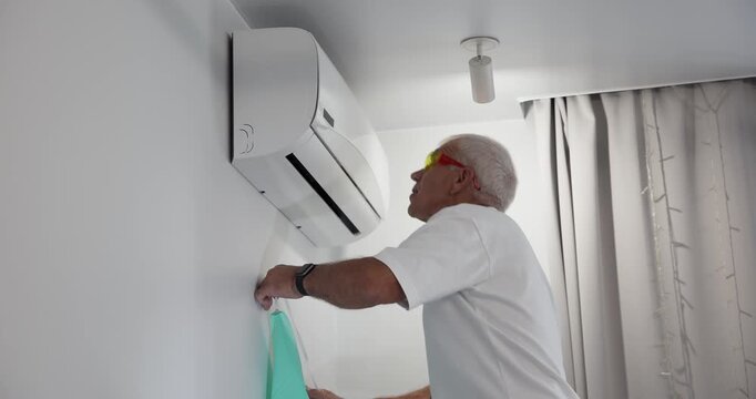 Tracking shot of senior technician removing air conditioner cover in home living room during daytime handheld pan and tilt.