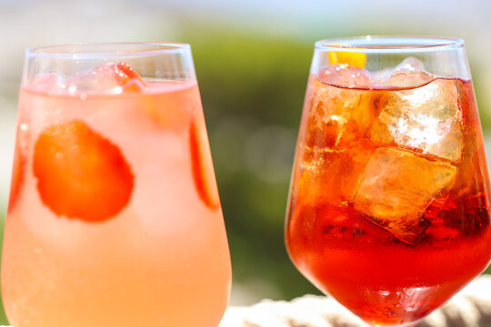 Two colorful cocktails with ice and fruit slices sparkle in bright sunlight, evoking summer refreshment and Mediterranean leisure in a vibrant outdoor setting.