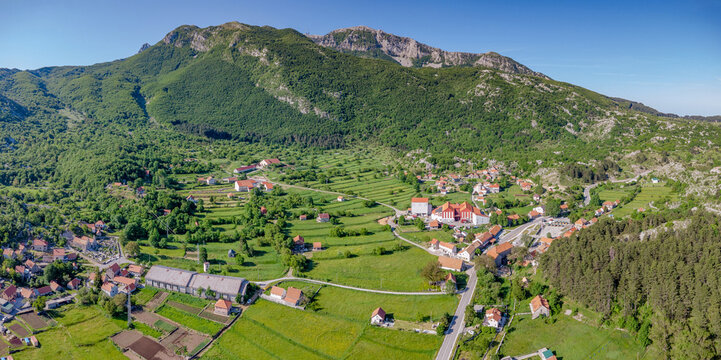 Njegusi village showcasing traditional houses, roads, and vibrant green agricultural fields from an aerial perspective in rural Montenegro