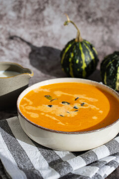 Bowl of creamy pumpkin soup topped with pumpkin seeds. Rich orange puree is served in rustic bowl and decorated with crunchy seeds creating an appetizing autumn meal presentation. Concept of seasonal
