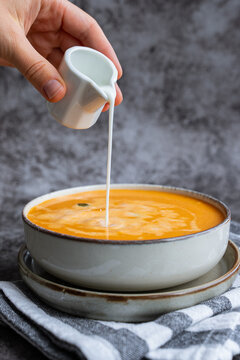 Smooth texture natural colors and fresh dairy contrast beautifully with the garnish of Creamy Pumpkin Soup Garnished with Pumpkin Seeds Cream Pouring by Hand. Concept of homemade cooking seasonal