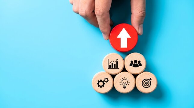 Hand placing wooden block with arrow icon on top of a business pyramid structure featuring strategy and growth symbols today.