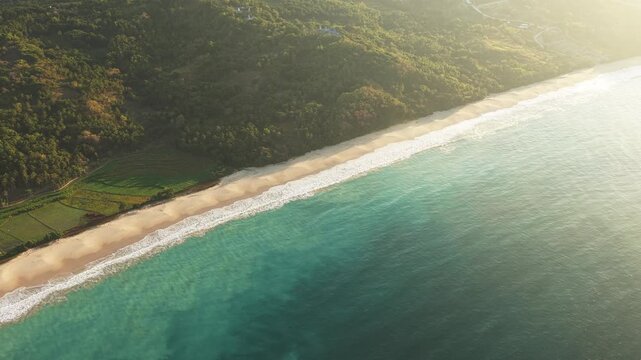 Aerial view of Pantai Rua beach with turquoise waves, sandy shore, and lush green hills in Kecamatan Wanokaka, Nusa Tenggara Timur, Indonesia.