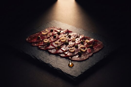 Beef Carpaccio Plated on Slate in Dramatic Moody Restaurant Lighting