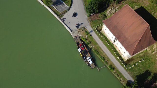 Top down aerial view of cars driving off a small cable ferry as it docks on the bank of the river Danube near Haibach ob der Donau, Upper Austria, on a sunny summer day. Shot on August 7, 2026.