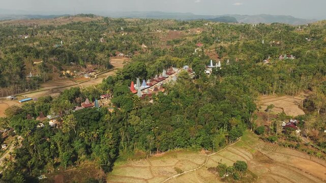 Aerial view of Kampung Prai Ijing featuring traditional thatched roof houses nestled among lush tropical trees and terraced fields in Kota Walkabubak, East Nusa Tenggara, Indonesia.