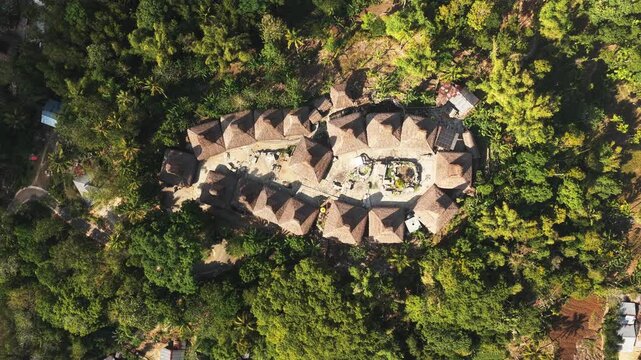 Aerial view of Kampung Prai Ijing traditional village with thatched roof houses surrounded by lush tropical forest in Kota Walkabubak, East Nusa Tenggara, Indonesia.