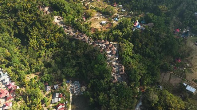Aerial view of Kampung Prai Ijing traditional village with distinctive high-roofed houses nestled in lush green hills and dense forest in Kota Walkabubak, East Nusa Tenggara, Indonesia.