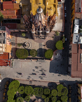 Aerial view of Parroquia de San Miguel Arcangel with pink spires, surrounded by the main square, manicured trees, and historic architecture in San Miguel de Allende, Guanajuato, Mexico.