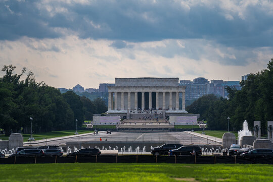 View of the Lincoln Memorial with its iconic columns and steps, surrounded by green lawns and a reflecting pool under a cloudy sky in Washington, District of Columbia, United States.