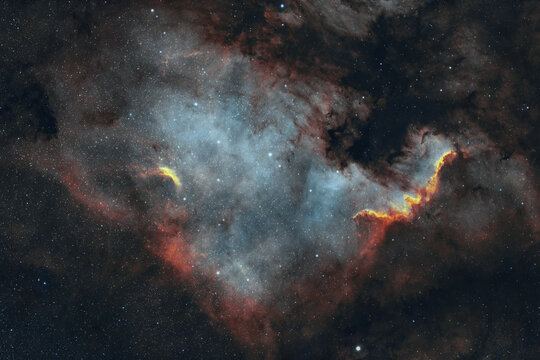 View of the North America Nebula, a vibrant emission nebula featuring glowing red and blue ionized gas clouds set against a dense field of stars over Poland.