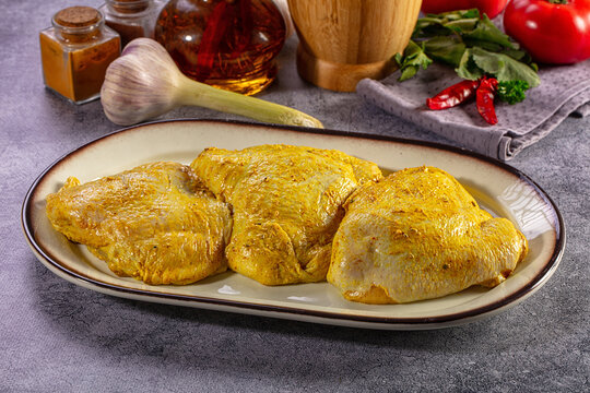 Raw seasoned chicken thighs on ceramic plate with spices and herbs