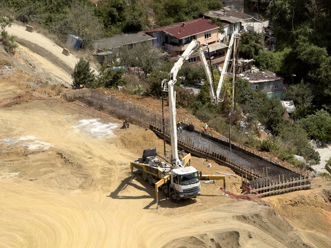 View of a concrete pump truck operating at a construction site on a hillside with workers and residential houses in the background in Sariyer, Istanbul, Turkiye.