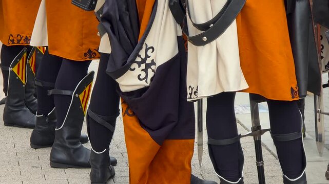 Mid section slow motion shot of participants wearing detailed medieval knight costumes with leather belts, bracers and embroidered tunics during Moros y Cristianos festival parade, horizontal 4K.