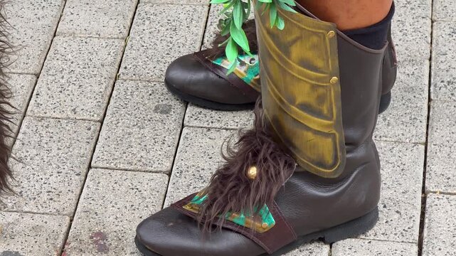 Close up slow motion shot of medieval style leather boots with brass greaves, fur trim and patina plates walking on cobblestone street during Moros y Cristianos festival parade, horizontal 4K.