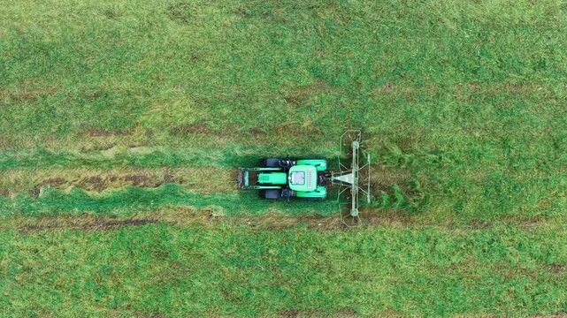 Aerial view of a green tractor with a hay rake harvesting grass in a field in Sylte, More og Romsdal, Norway.