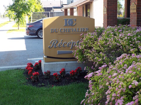 Gatineau, Quebec, Canada &ndash; June 24, 2026: A golden sign reading "DU CHEVALIER R&eacute;ception" stands amidst vibrant pink flowering bushes near a parking area on Bd Gr&eacute;ber.