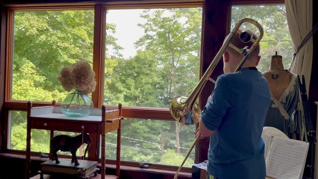 Young boy practicing the trombone indoors near a window