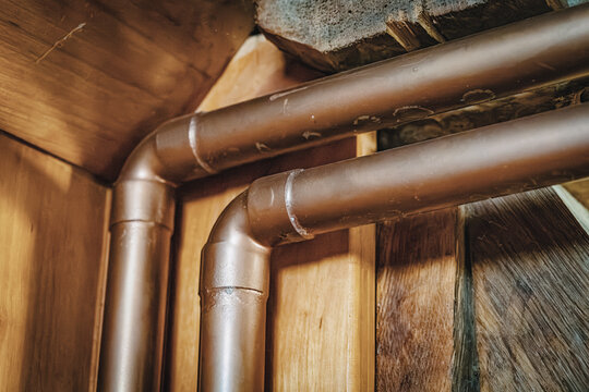 copper pipes bending at a corner joint inside a rustic timber-framed basement, evoking old-world craftsmanship and warmth.