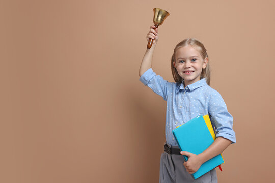 Little girl with notebooks ringing school bell on color background. Space for text