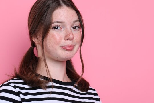Beautiful teenage girl with freckles on pink background, space for text