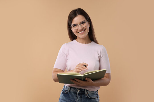 Happy teacher with notebook and pen on beige background