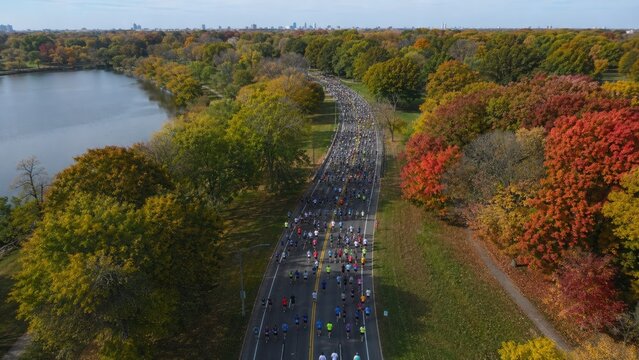 Aerial view of a large autumn road race winding through a colorful park beside a lake