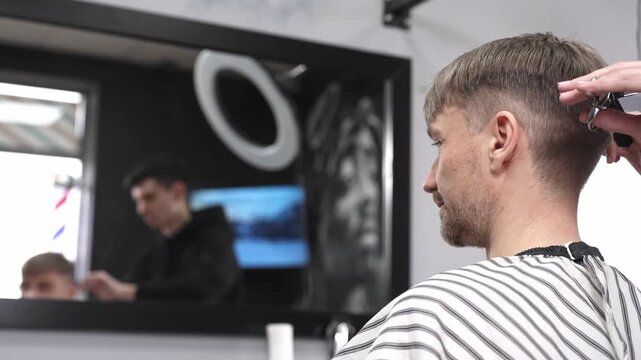 Professional barber trimming male client's hair with scissors and comb, creating precise modern hairstyle inside contemporary grooming salon