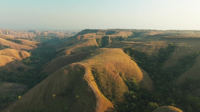 Aerial view of Hars Garden Sumba featuring rolling savanna hills and lush valleys under soft golden hour light in Pandawai, East Nusa Tenggara, Indonesia.
