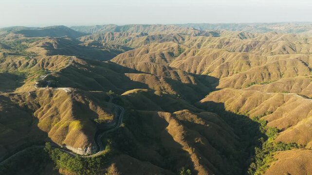 Aerial view of Palindi Piarakuku Hills with a winding road cutting through the golden grassy slopes in Matawai La Pawu, East Nusa Tenggara, Indonesia.