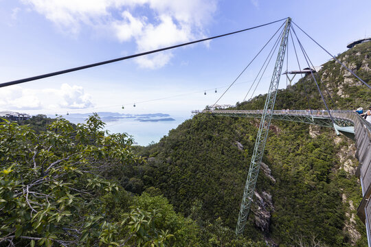 View of the Langkawi Sky Bridge, a curved pedestrian bridge suspended above lush green mountains with a view of the sea and cable cars in Langkawi, Kedah, Malaysia.