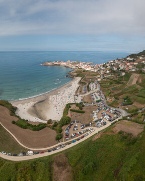 Aerial view of the coastal town of Caion featuring a sandy beach with many visitors, surrounding green fields, and busy parking lots in Caion, A Coruna, Spain.