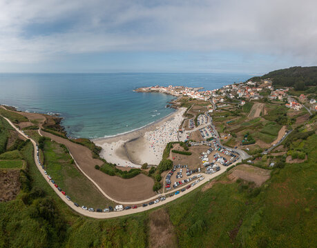 Aerial view of the coastal town of Caion with its sandy beach, turquoise Atlantic waters, and busy parking areas surrounded by green hills in Caion, A Coruna, Spain.