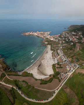 Aerial view of the coastal town of Caion featuring a sandy beach, turquoise ocean waters, and surrounding green fields in Caion, A Coruna, Spain.